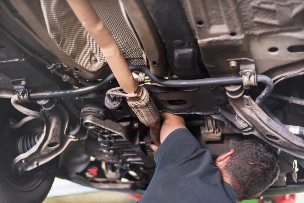 Technician working on a vehicle's exhaust system from underneath on a lift