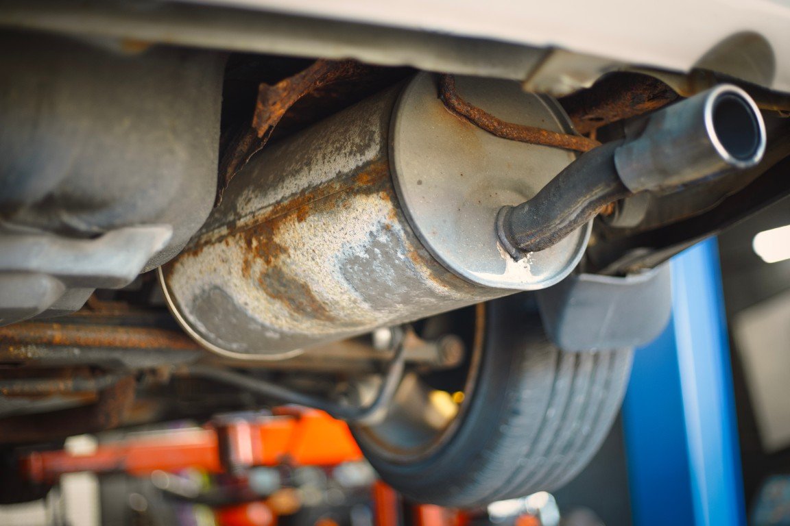 Heavily rusted exhaust pipe and muffler seen from under a vehicle on a lift