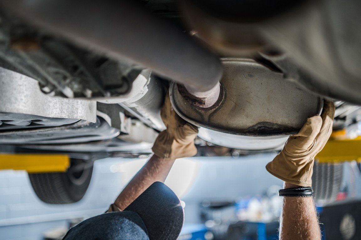 Technician in gloves working on an exhaust system beneath a raised vehicle