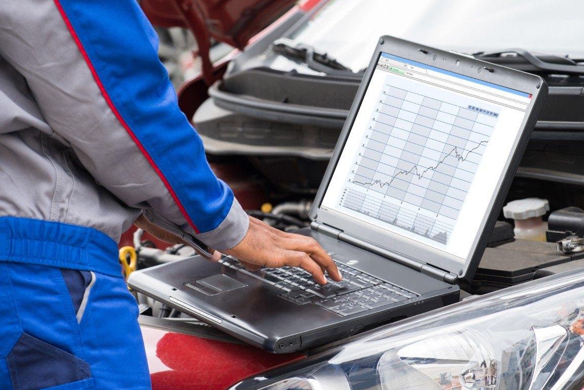 Technician running diagnostics on a laptop connected to a car