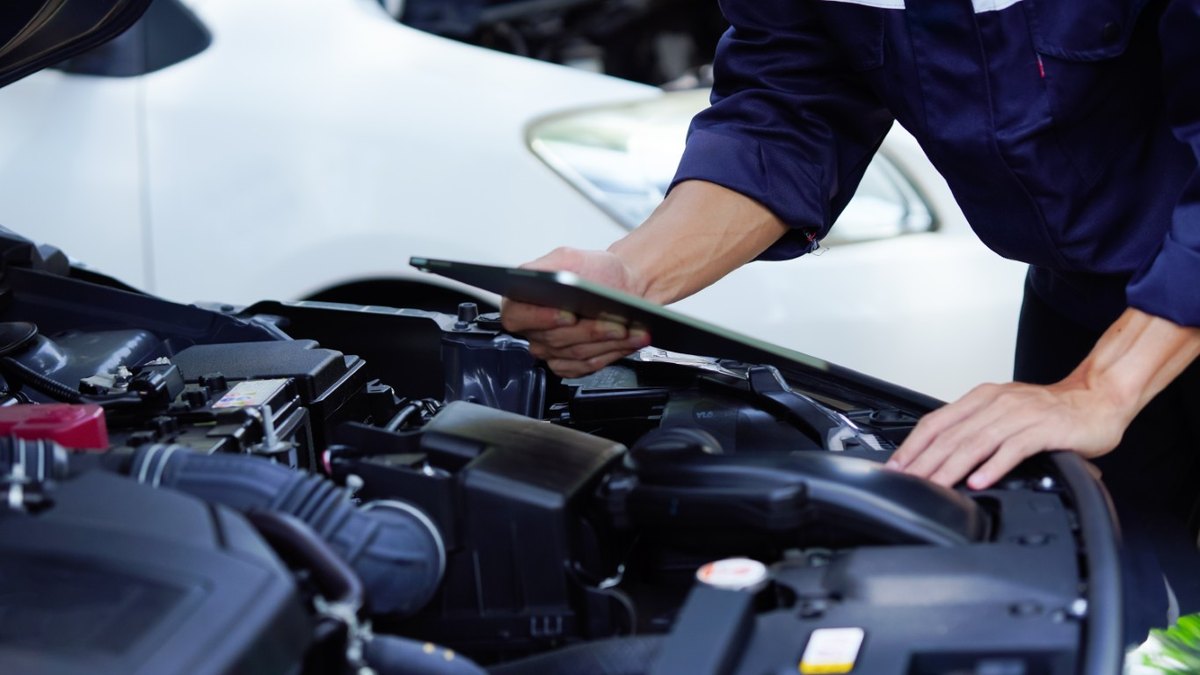 Technician with an inspection clipboard leaning over the engine bay of a car in a repair shop