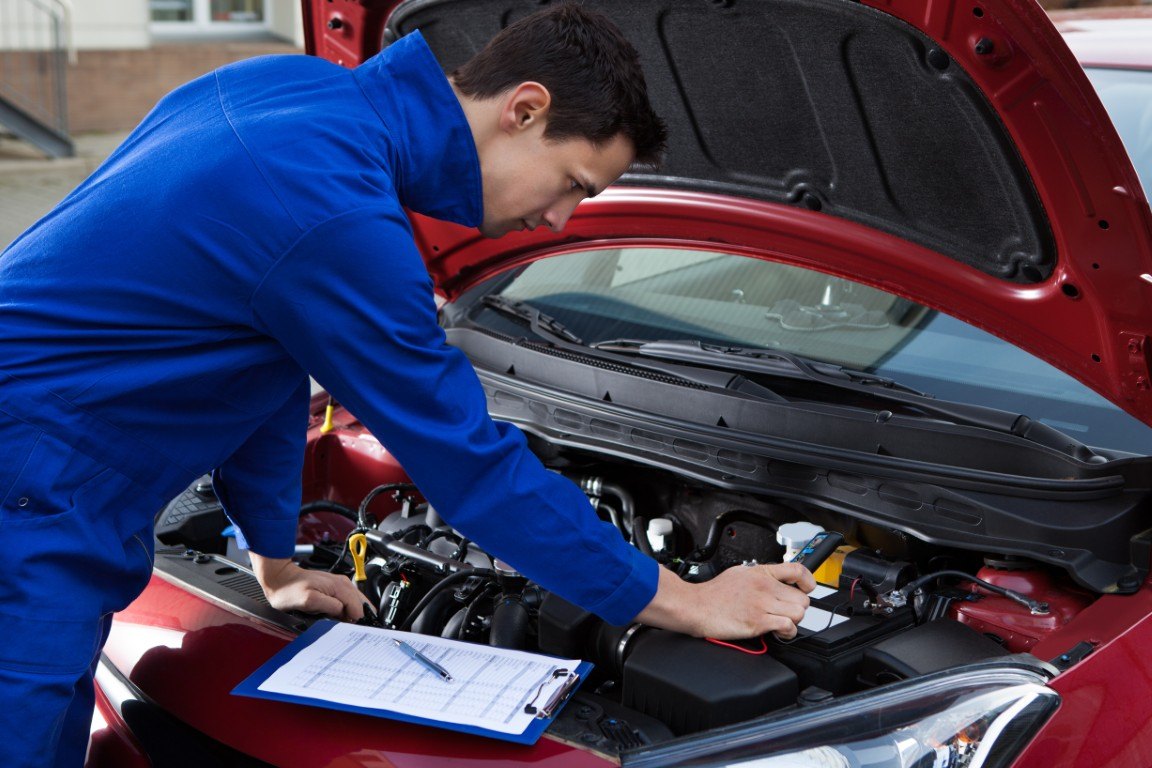 Technician in work overalls servicing a vehicle in a repair shop bay